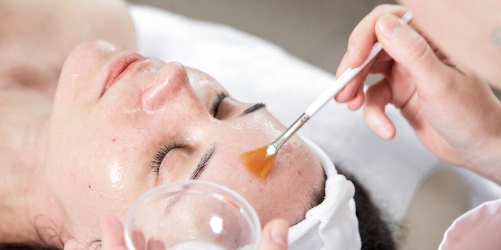Facial peeling, skin treatment. A dermatologist applies of phytic acid with a white fan brush on female face. A caucasian woman in cosmetic clinic. Cosmetology, facial skin care. Girl in beauty salon